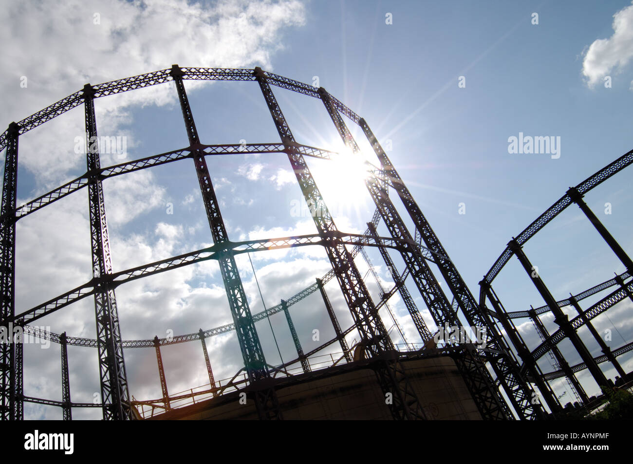 London Gas towers standing blackly against a blue cloudy sky lit up by flared sunlight Stock