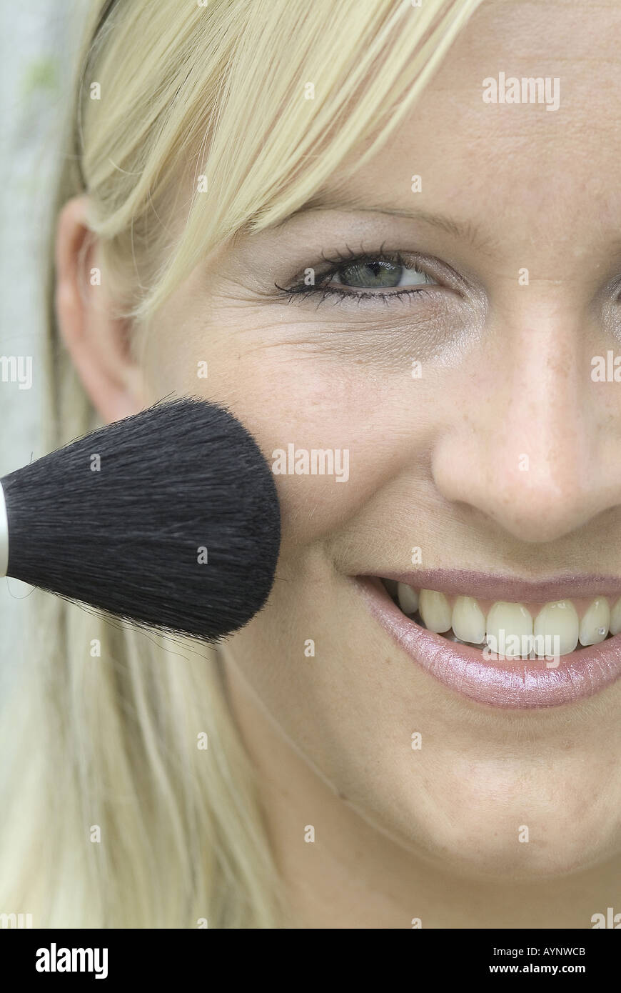 Blonde Frau pudert sich das Gesicht mit einem Pinsel Stock Photo