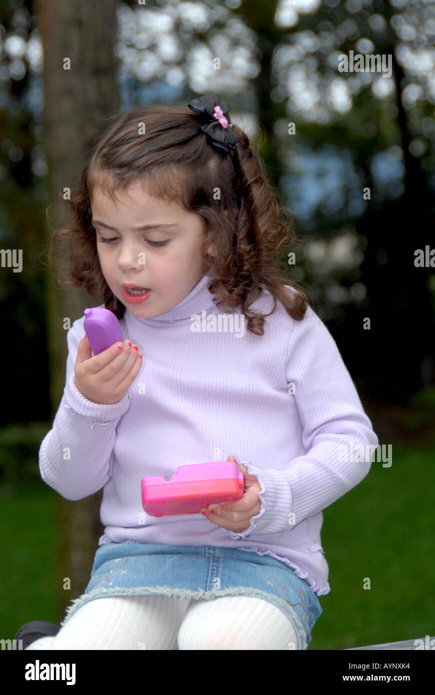 Three year old girl seated on an outdoor bench studying a toy telephone Stock Photo