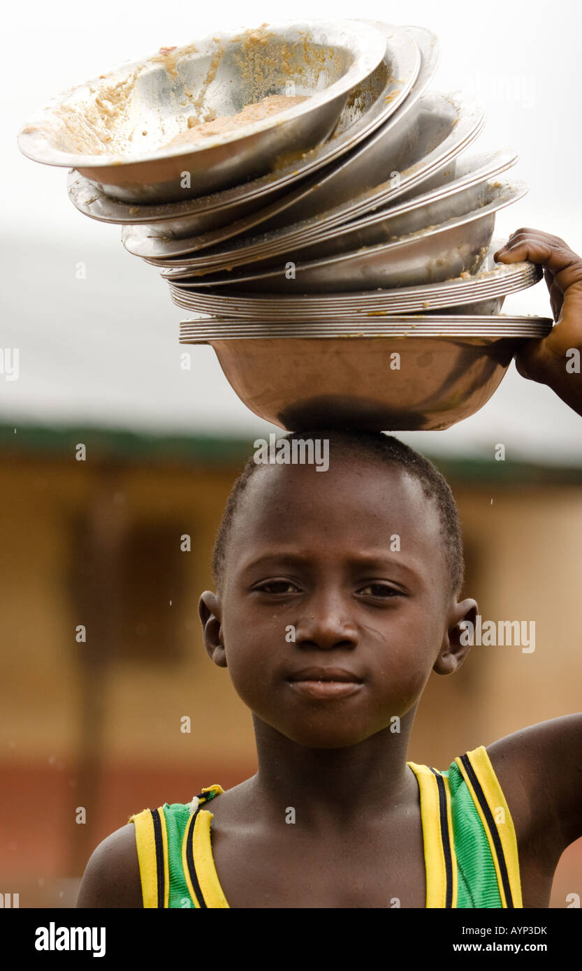 A boy carries dirty metal bowls used for lunch on his head Stock Photo
