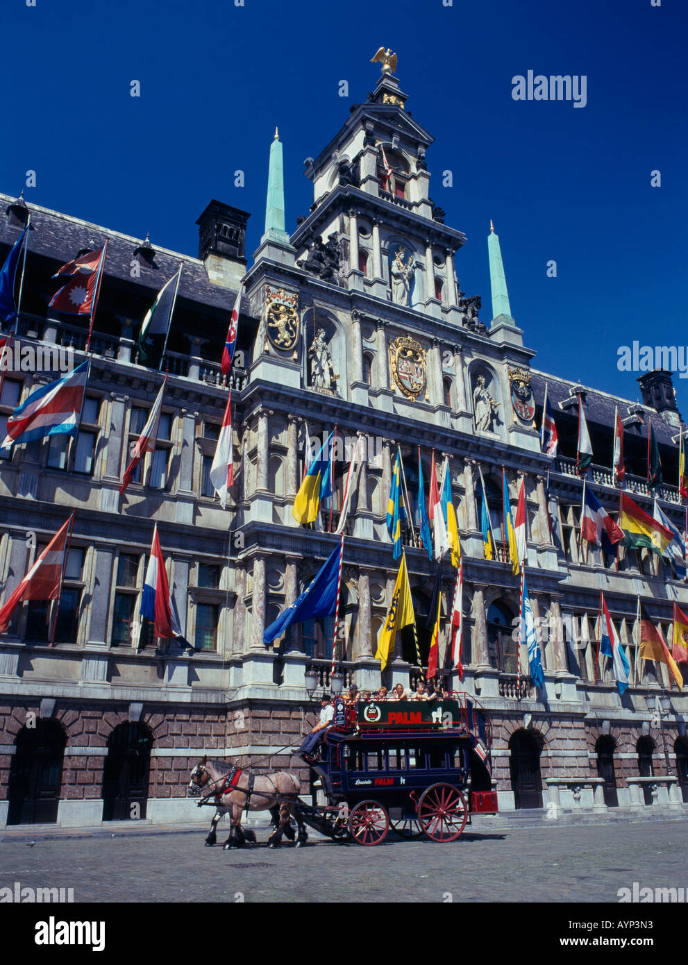 Belgium, Flemish Region, Antwerp.  Horse drawn tourist coach in front of the Town Hall which is covered in flags. Stock Photo