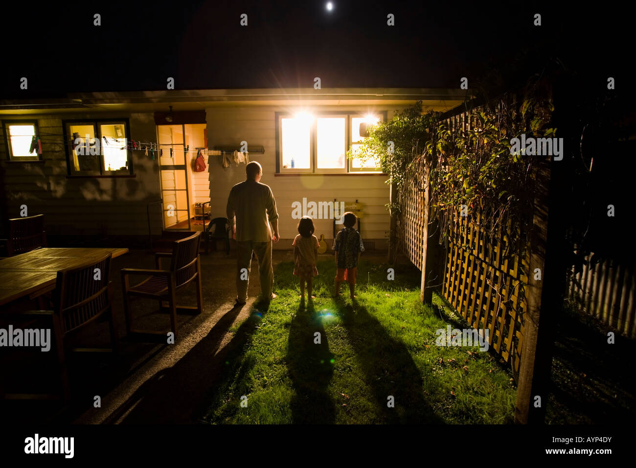 Standing in garden at night and watching through the window, a man, a girl aged four, a boy aged six Stock Photo
