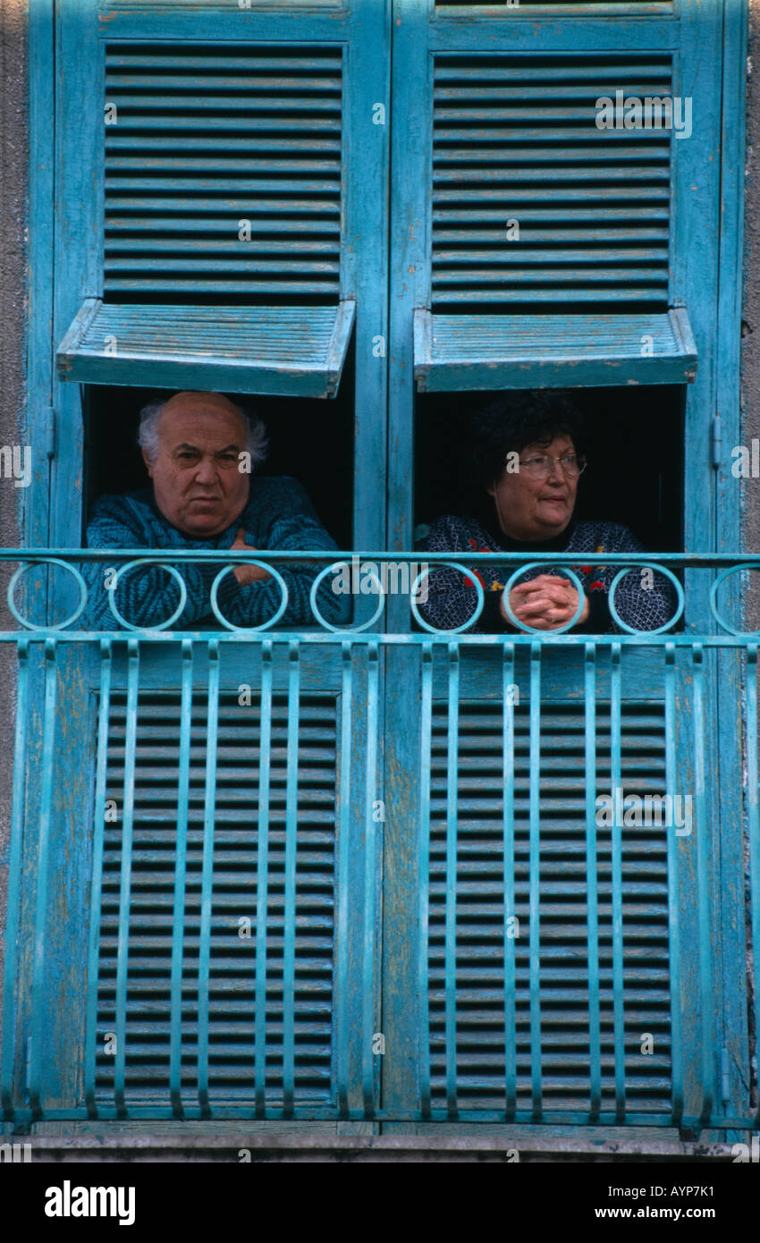 ITALY Campania Naples San Giorgio a Cremano Elderly couple looking out from turquoise open wooden window shutters above street Stock Photo