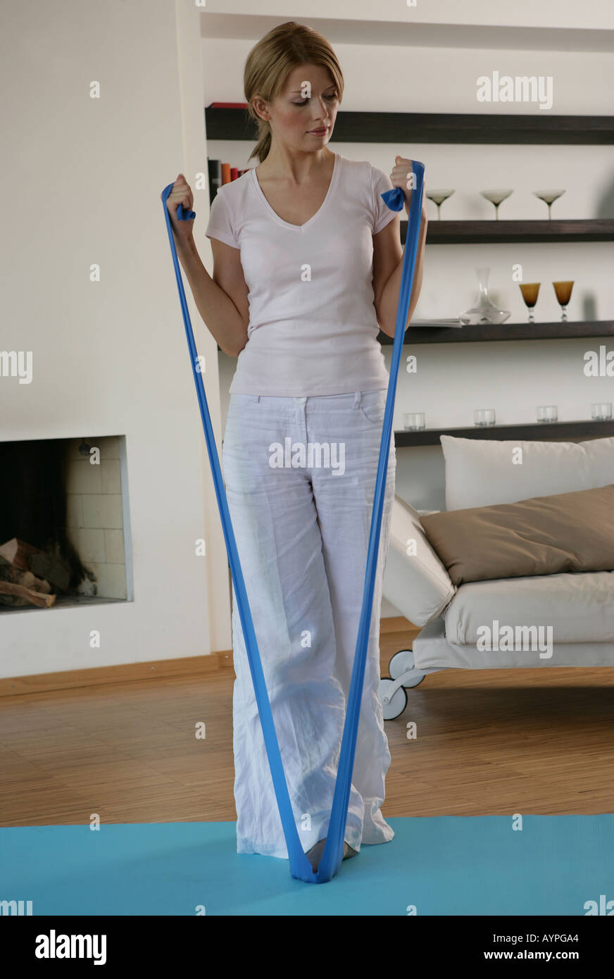 A blonde woman stretching a blue rubber band while exercising Stock Photo
