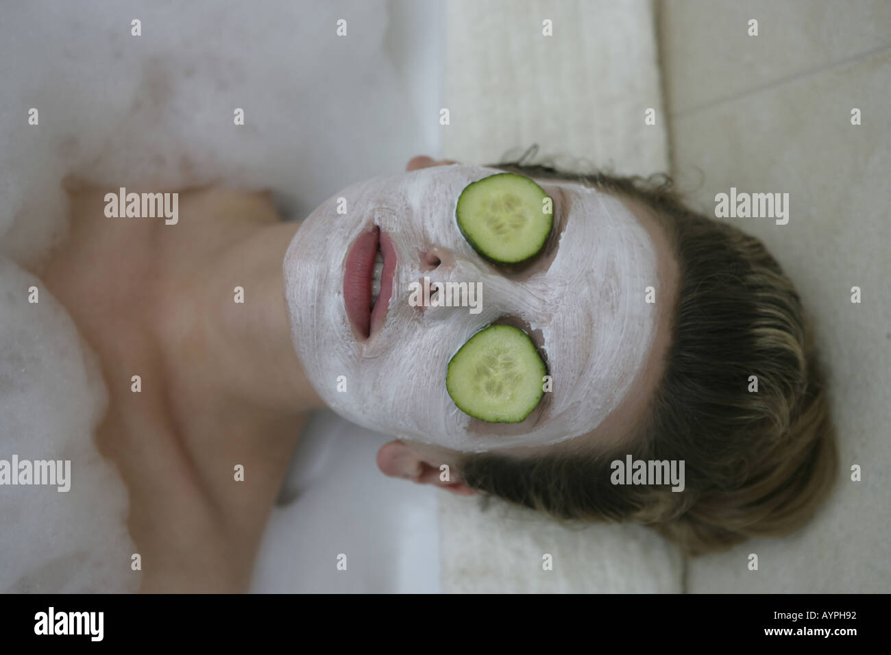 A woman relaxing in bathtub with cucumber slices on her eyes Stock Photo