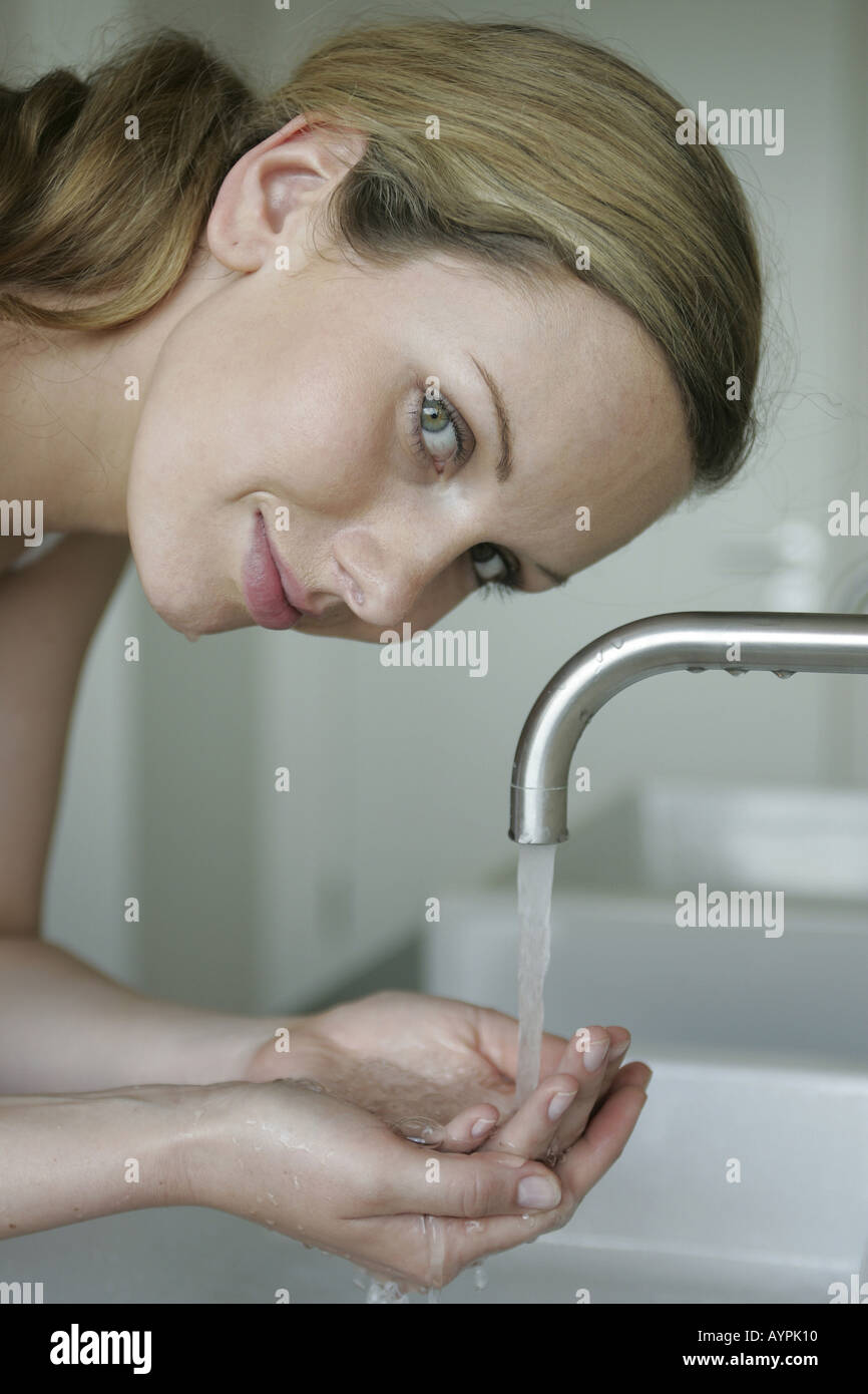 A blonde woman holds water in her palms as she smiles at the camera ...