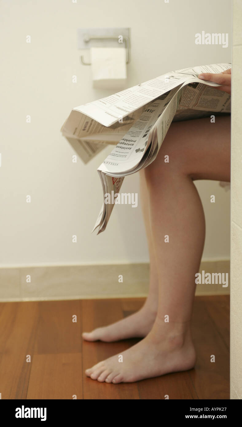 Legs of a woman seen as she sits on a water closet reading a newspaper Stock Photo