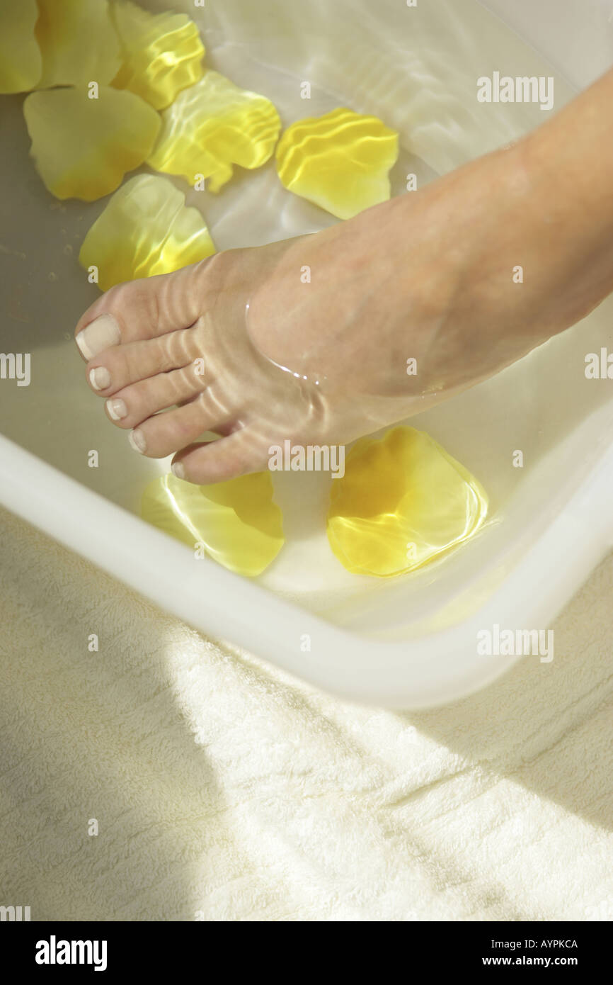High angle view of woman foot over a tub of yellow petals and water Stock Photo