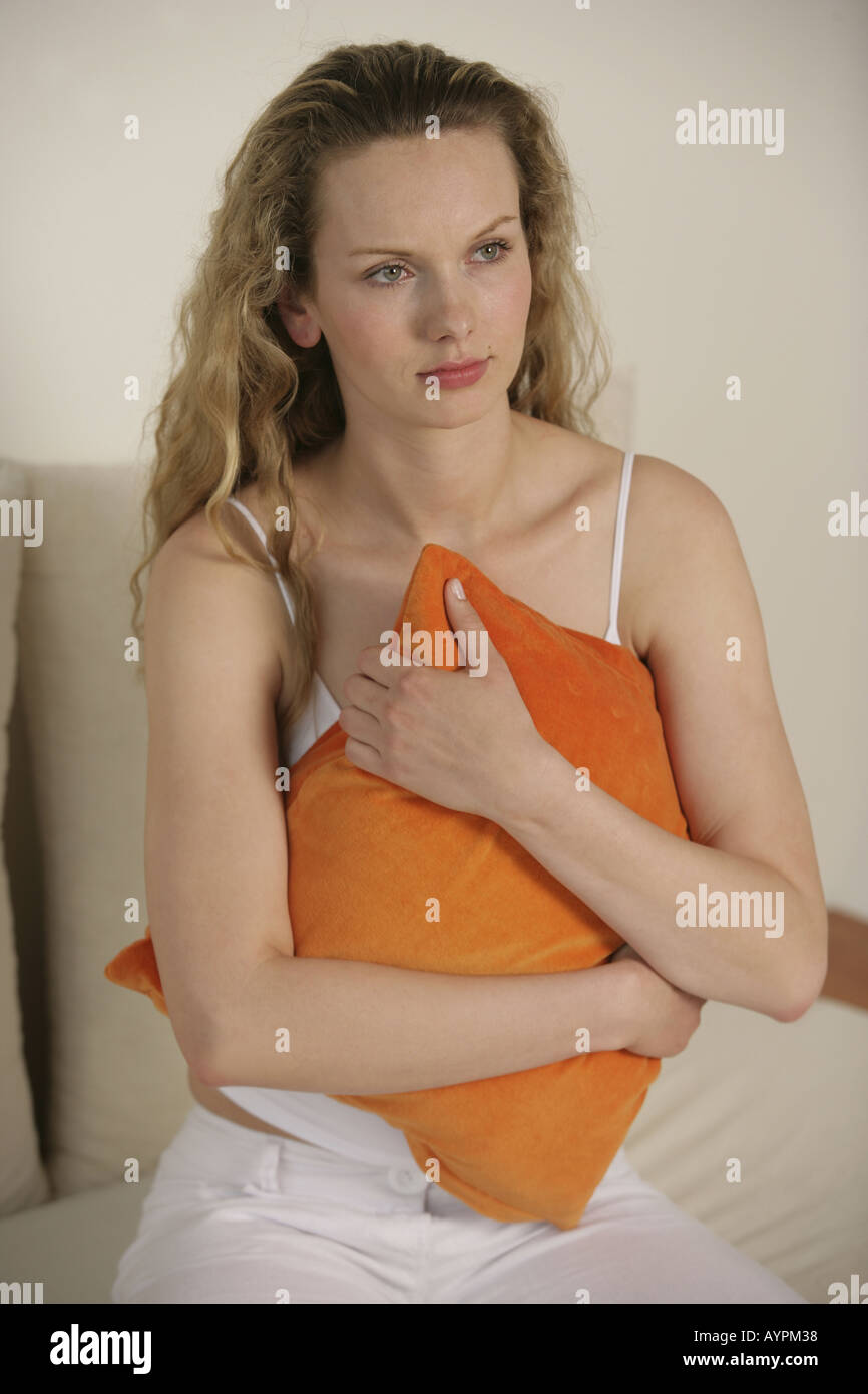 A side view of a blonde woman holding an orange pillow Stock Photo