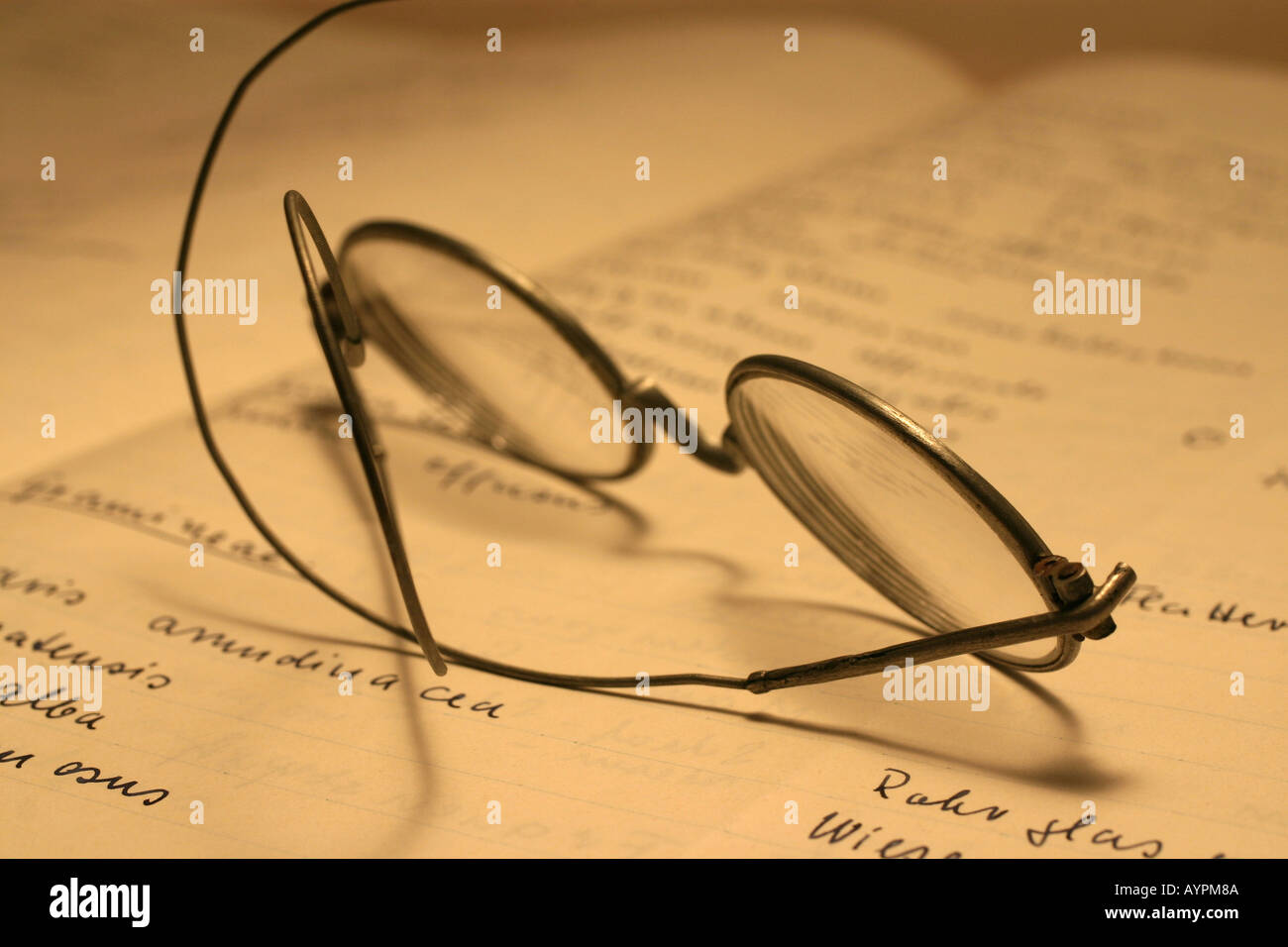 Blurred view of text seen on the book with spectacles kept on it Stock Photo