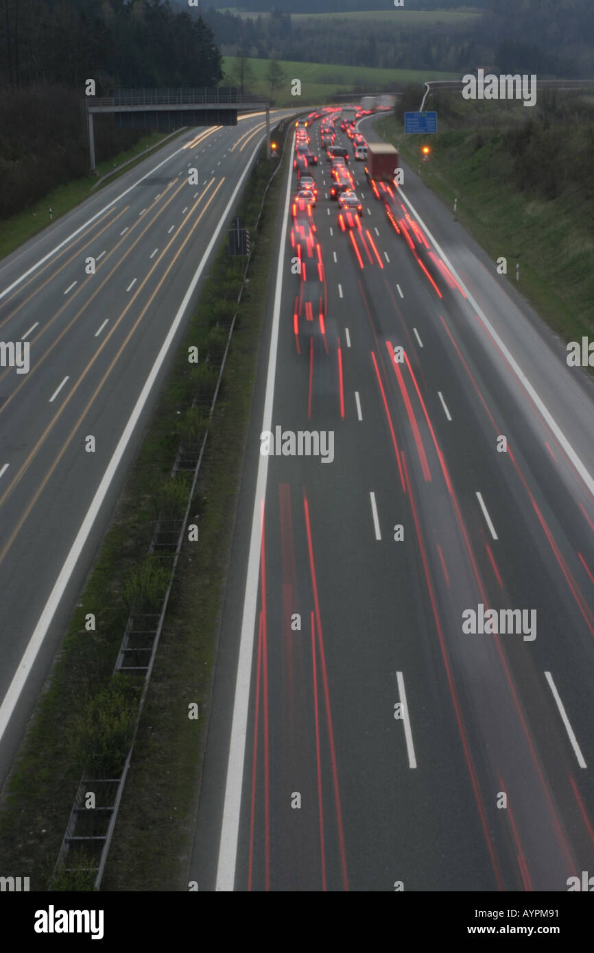 Trails of large group of vehicles seen speeding across the highway with trees and grass on either side Stock Photo