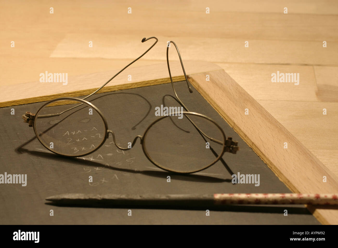 Circular framed spectacles kept on a slate beside a long pencil Stock Photo
