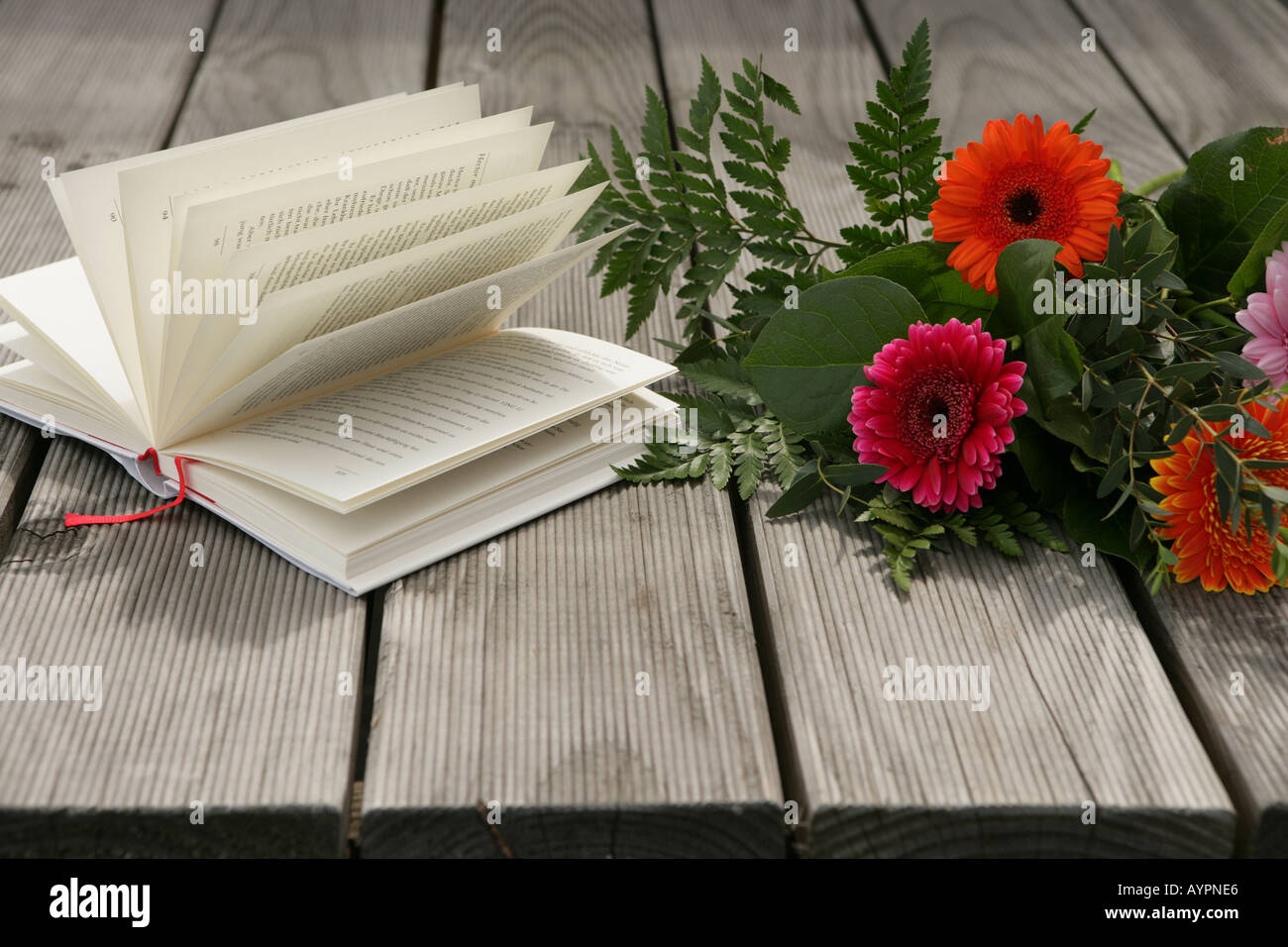 Bunch of flowers and a novel seen on a wooden table Stock Photo