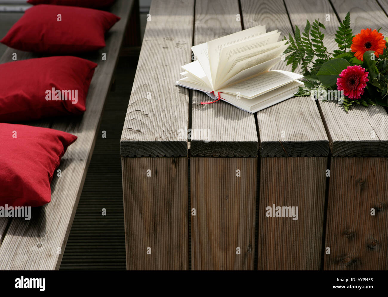 Bunch of flowers and a novel seen on a wooden table with some red cushions beside it Stock Photo