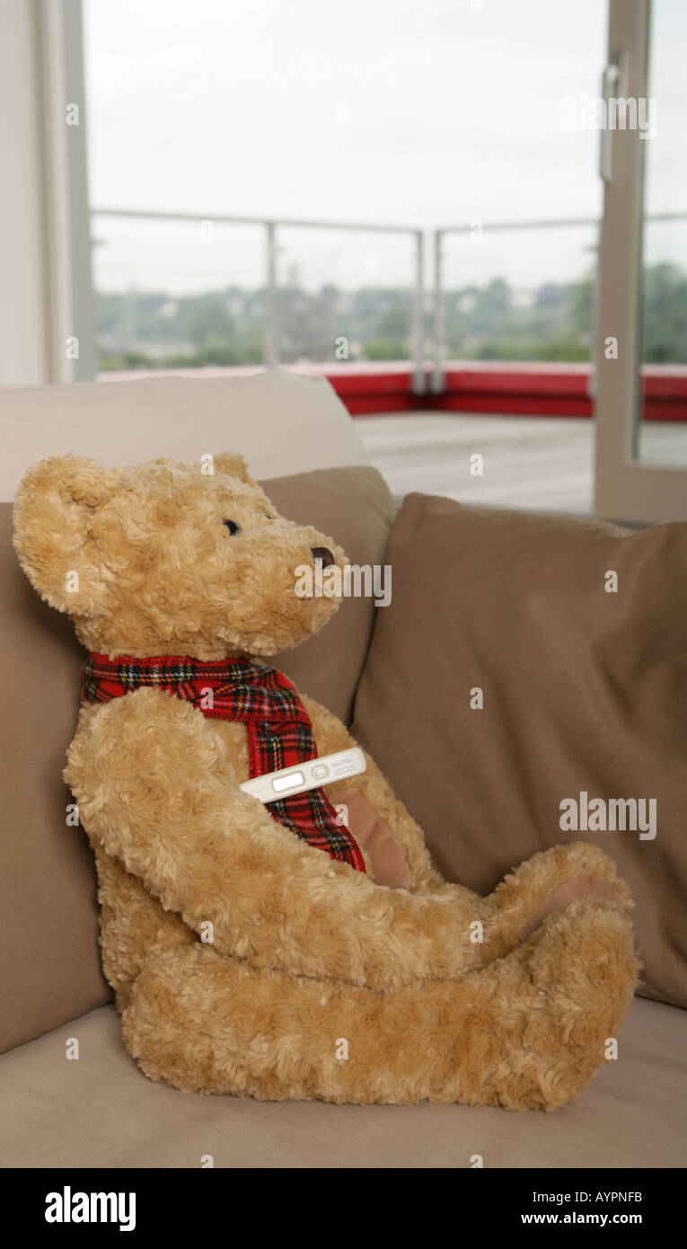 Teddy bear resting on a couch with a thermometer under its arms Stock Photo