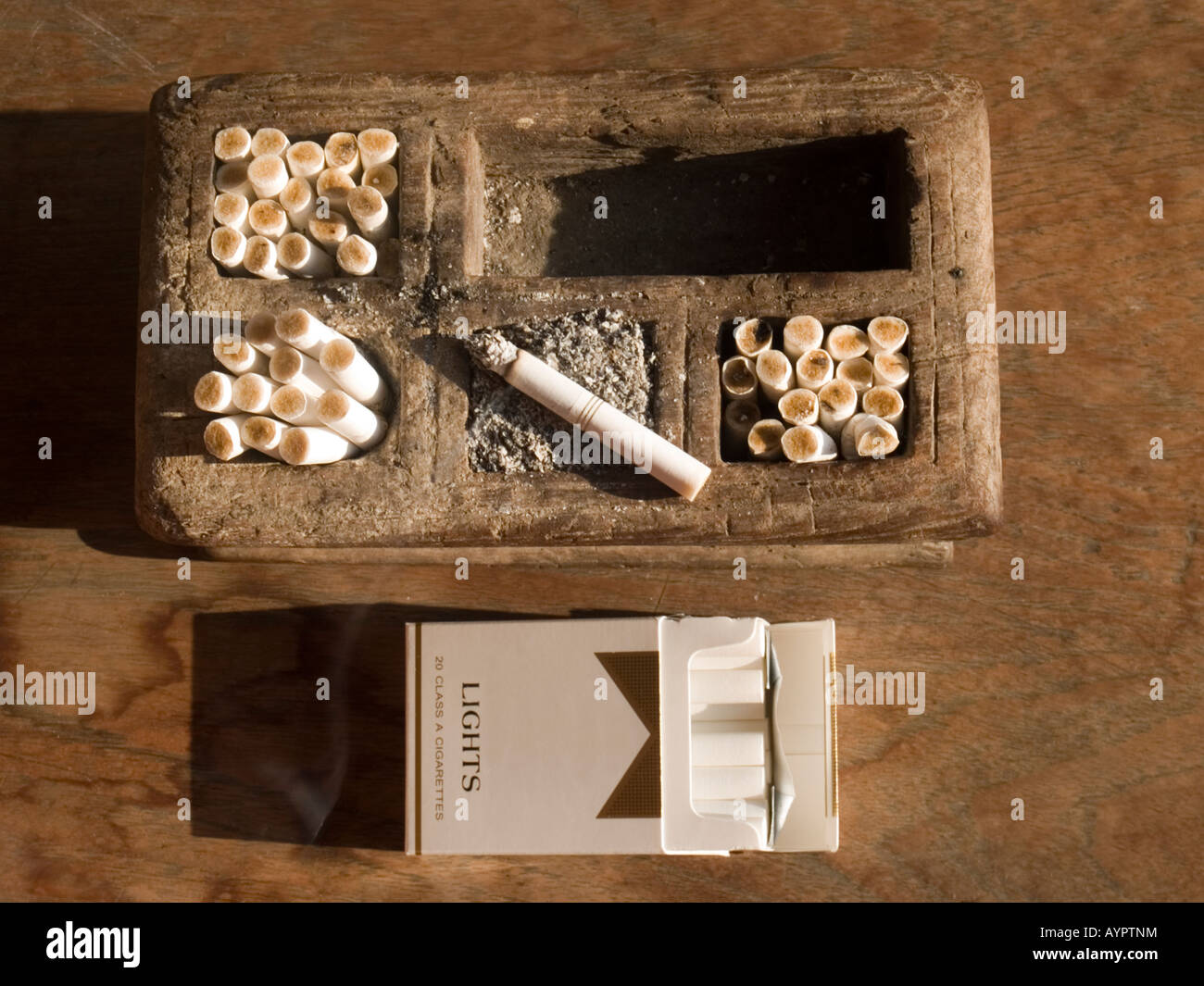 javanese tobacco Traditional wooden carved Javanese ashtray full of butts and ash with lit  cigarette on top Stock Photo