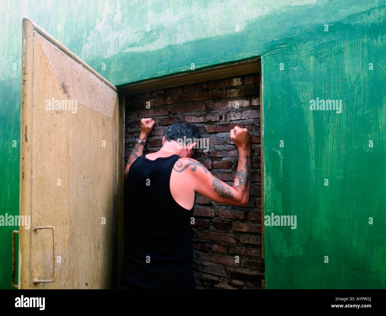 Man in open doorway banging fists against a brick wall that is