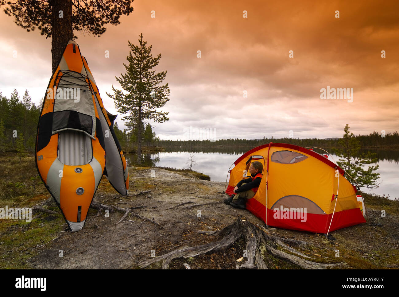 Two inflatable kayaks and a woman sitting in front of a tent at