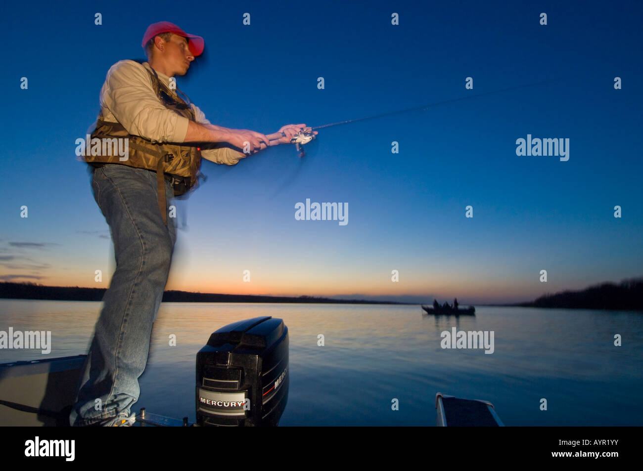A FISHERMAN FISHES FROM A BOAT FOR WALLEYES AT DUSK ON BIG STONE LAKE