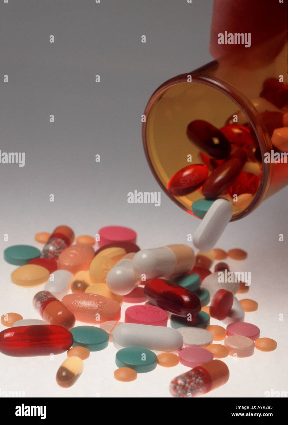 multi coloured pills being poured out of plastic pill bottle Stock Photo