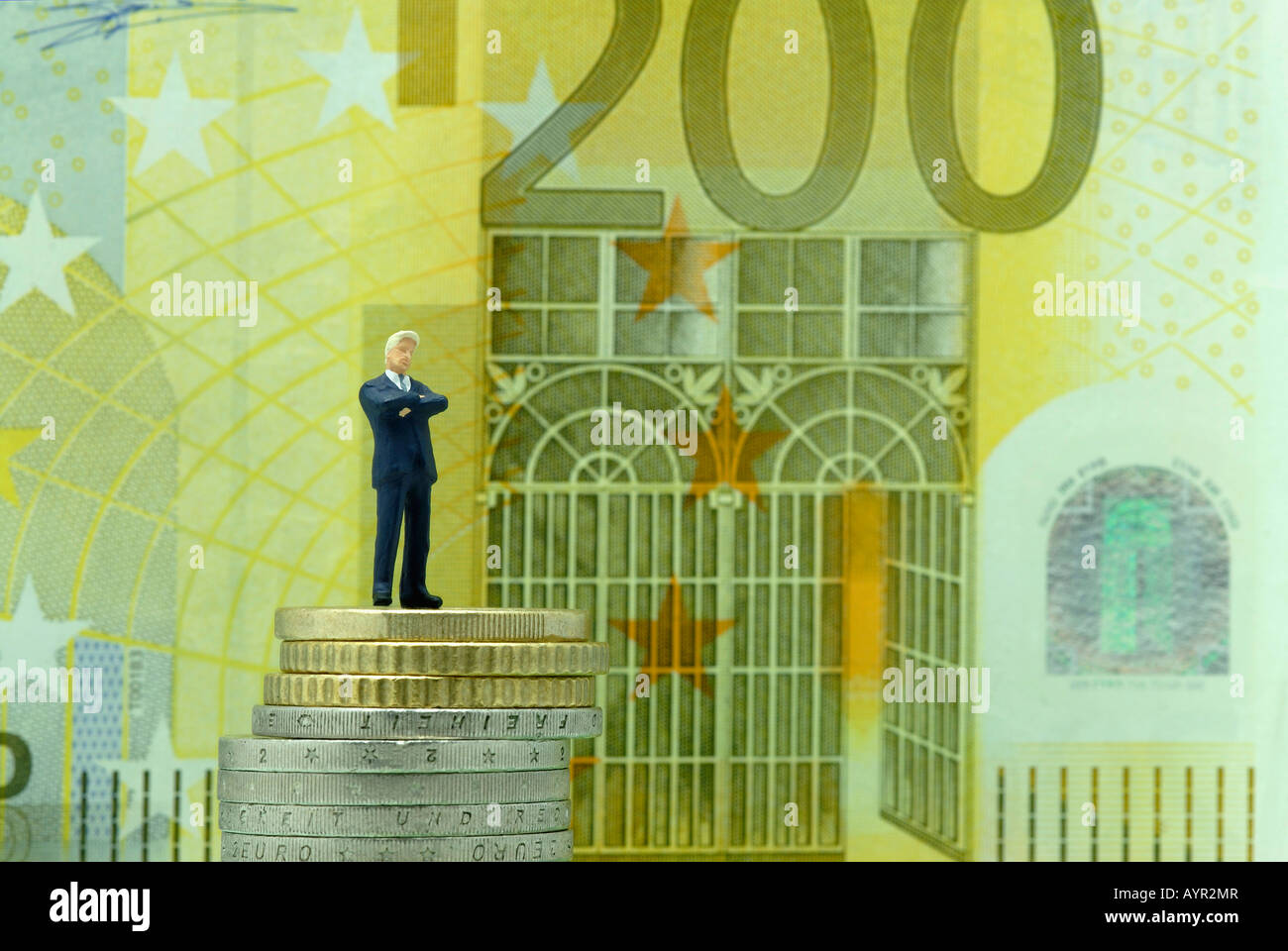 Satisfied-looking businessman standing on a stack of coins in front of a 200-Euro bill Stock Photo