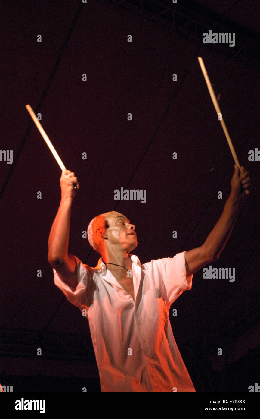Pedro Rosa, teacher of Afro Brasil dance, performing with drumsticks under red stage lighting. Stock Photo
