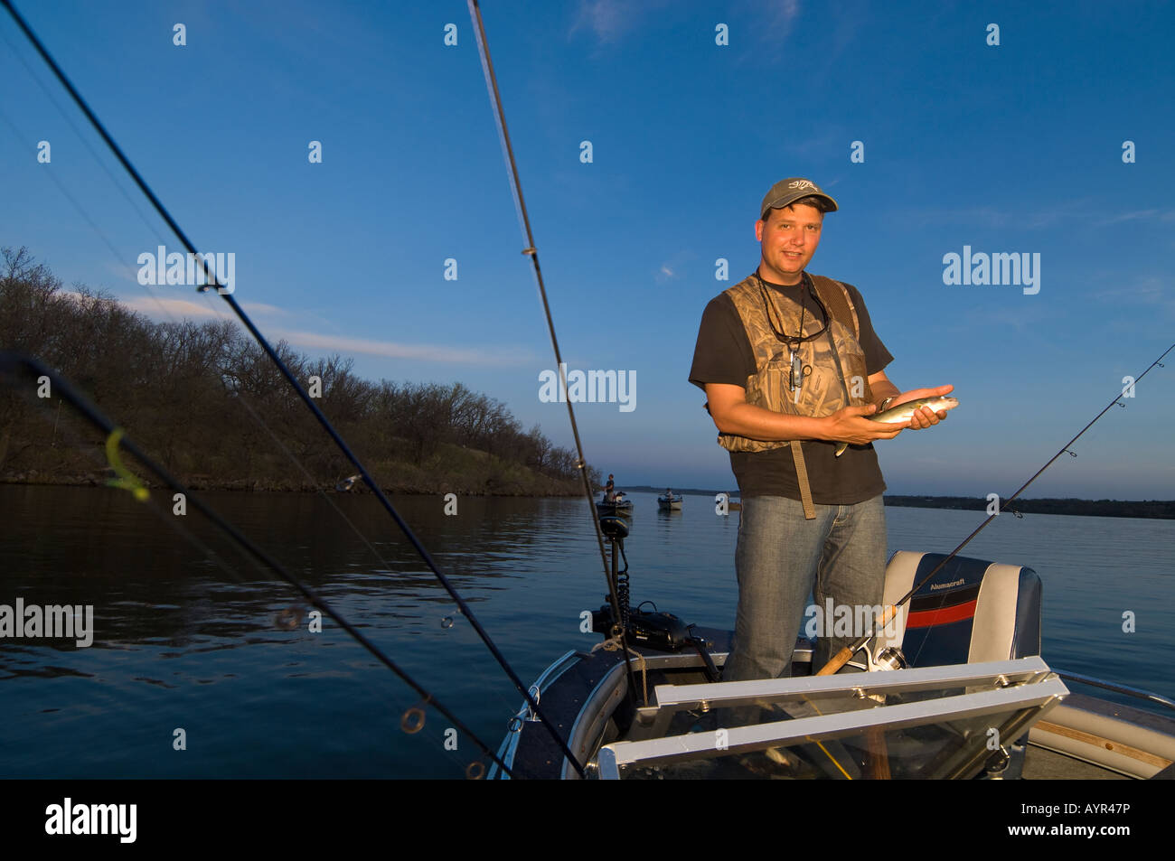 A FISHERMAN FISHES FROM A BOAT FOR WALLEYES AT DUSK ON BIG STONE LAKE