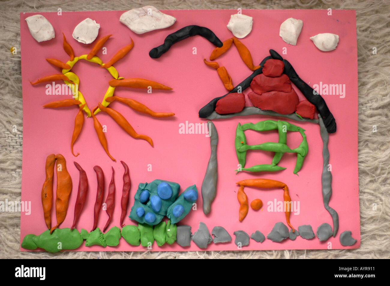 Colorful child's plasticine clay artwork of a sun house and garden on a pink background, featuring textured 3D modeling shapes. Stock Photo