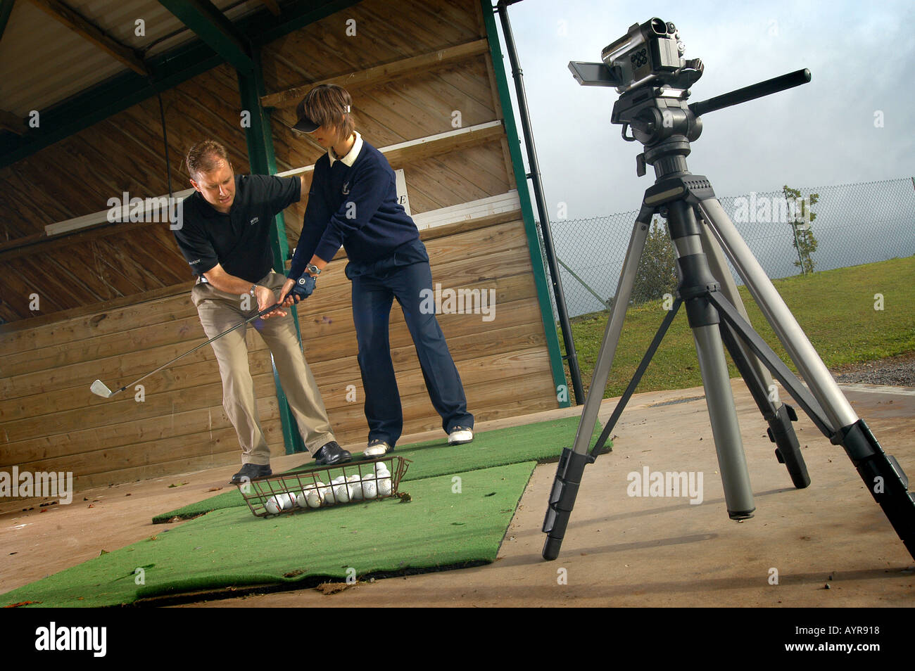 A golf professional and student in a driving range having a lesson and using camera equipment to