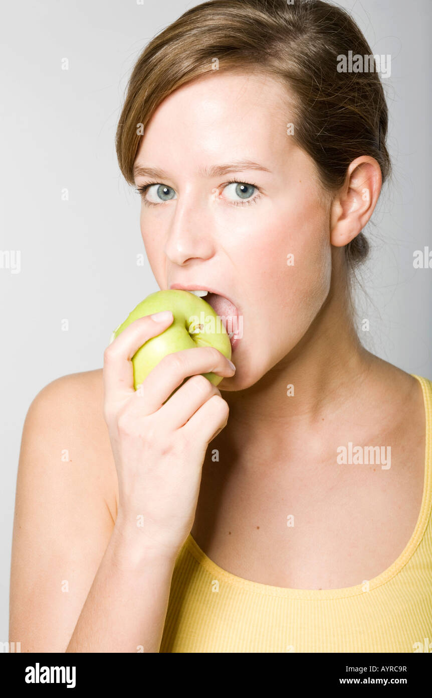 Young woman biting into a green apple Stock Photo