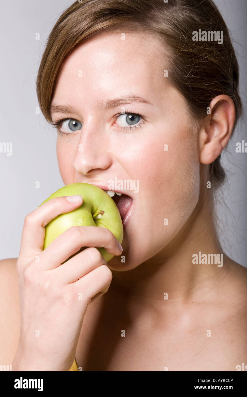 Young woman biting into a green apple Stock Photo