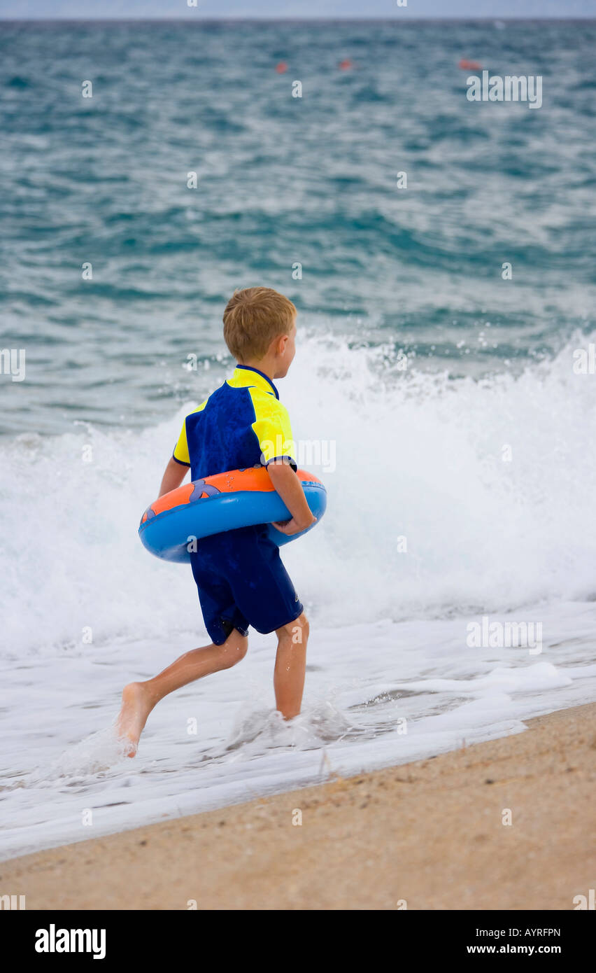 Fiveyearold boy wearing flotation tire and wetsuit running along the