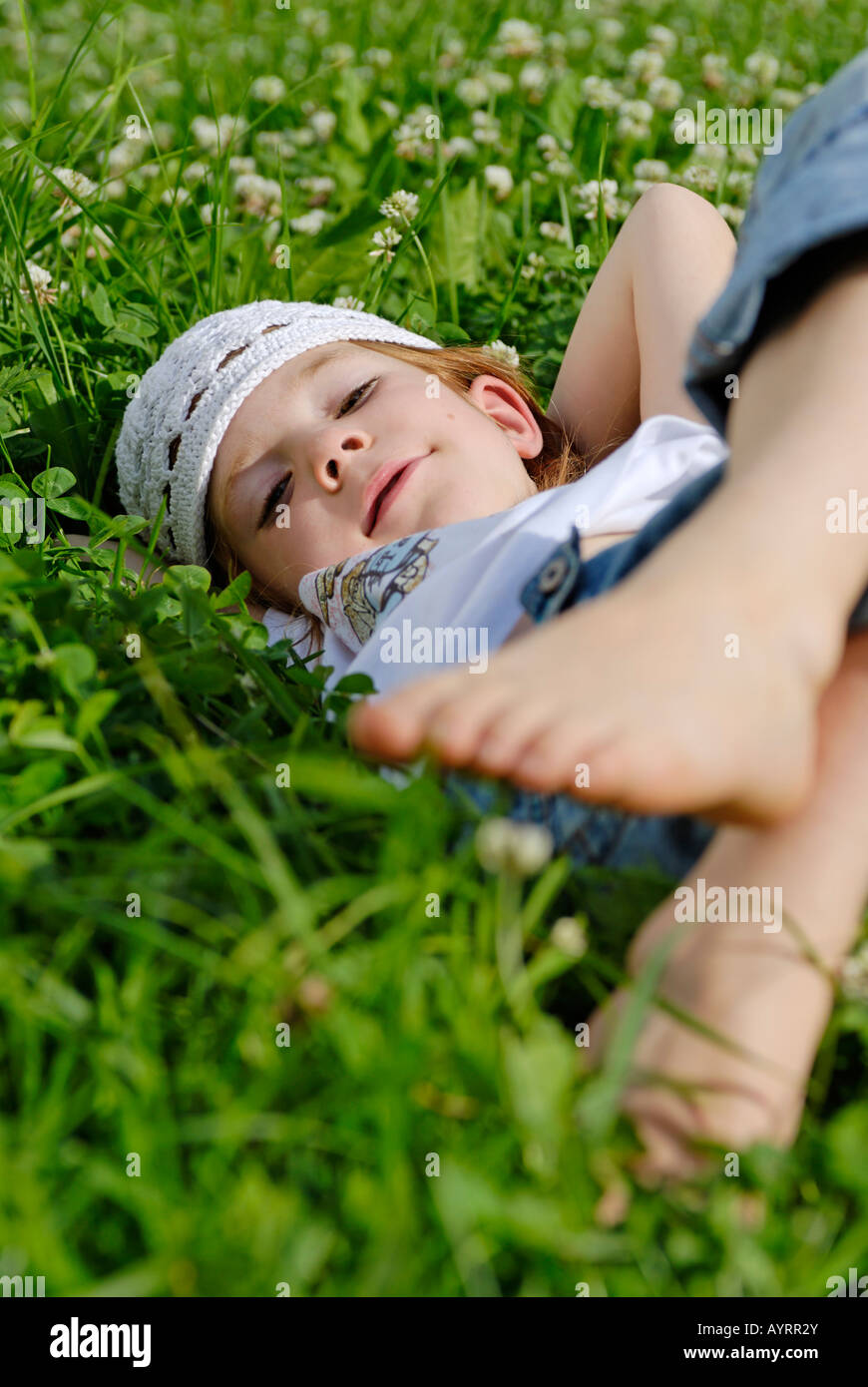 Girl laying on a cloverleaf meadow, daydreaming in summertime Stock Photo