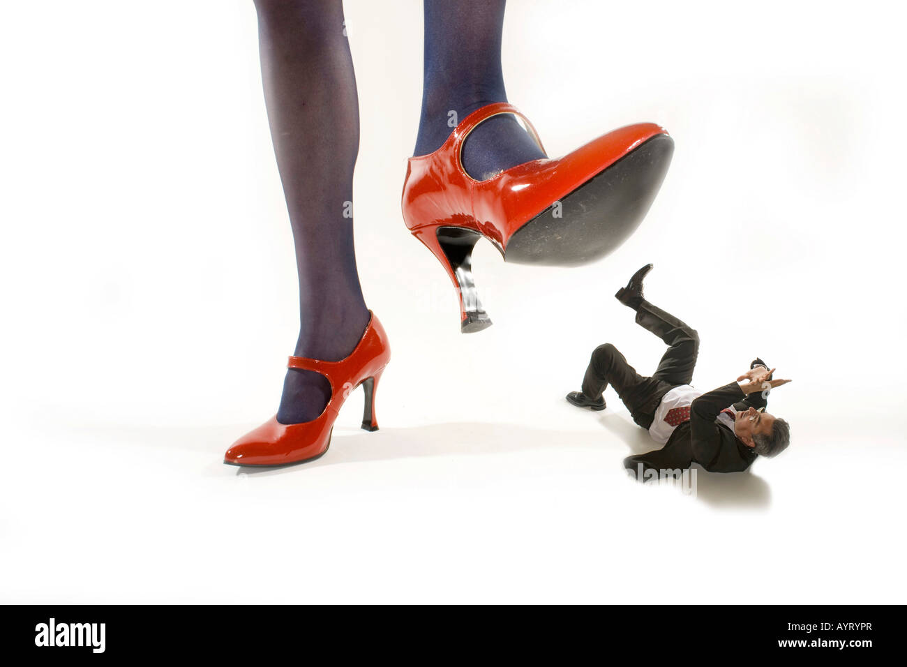 Woman in red high heels stepping on a shrunken man Stock Photo
