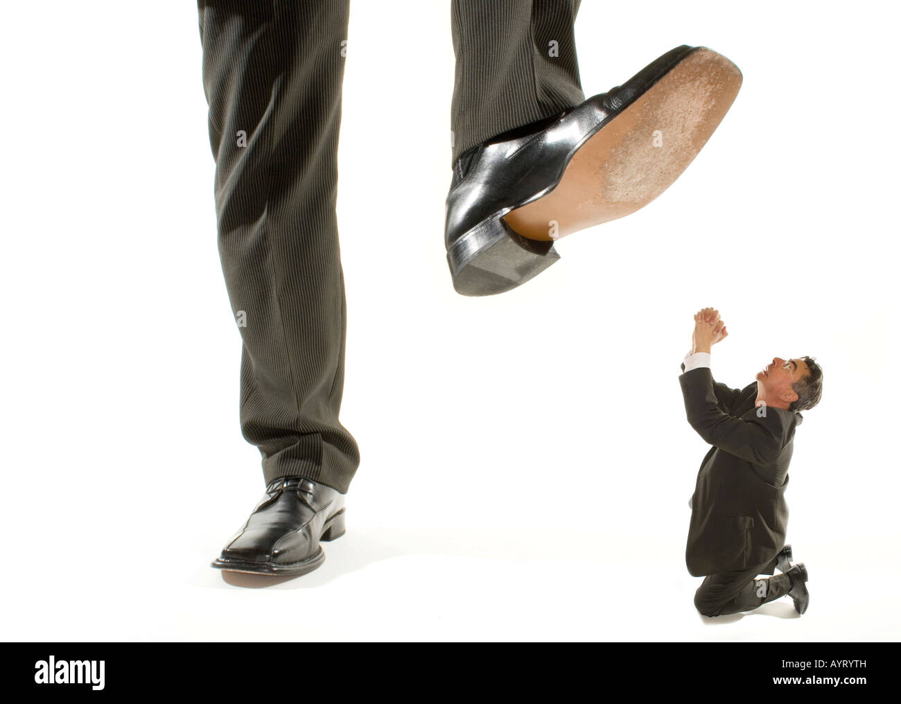 Giant foot stepping on a kneeling businessman praying for mercy Stock Photo