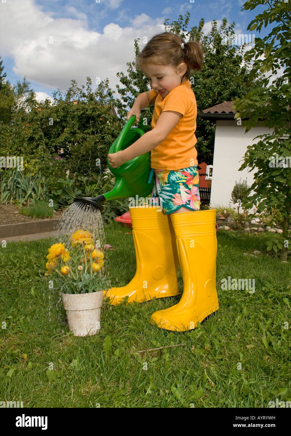 Girl watering her yellow flowers wearing yellow rubber boots Stock Photo