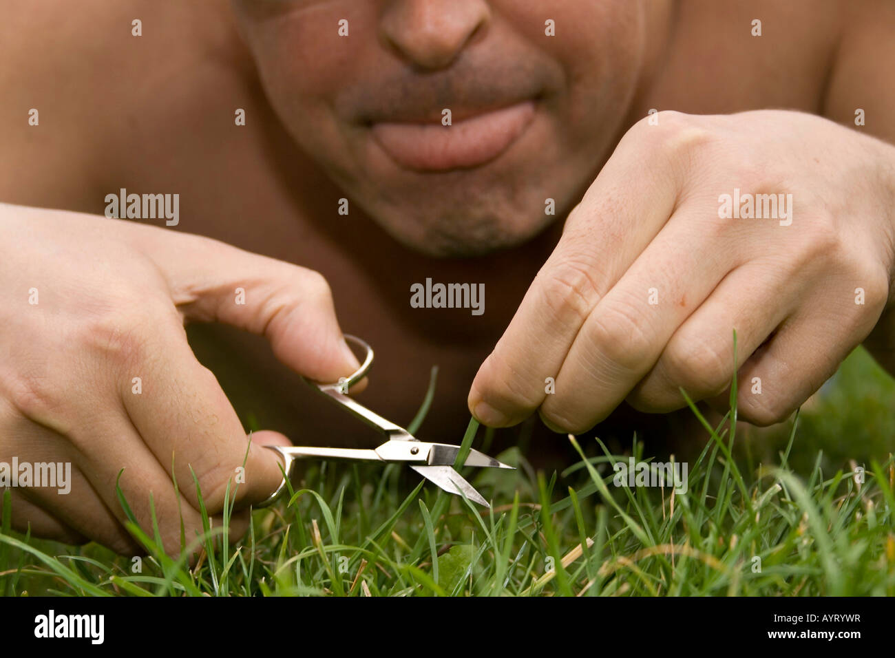 Man cutting grass on his lawn using nail scissors Stock Photo