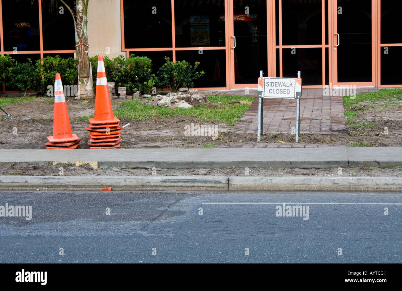 Orange cones in front of a building next to a sidewalk by the road Stock Photo