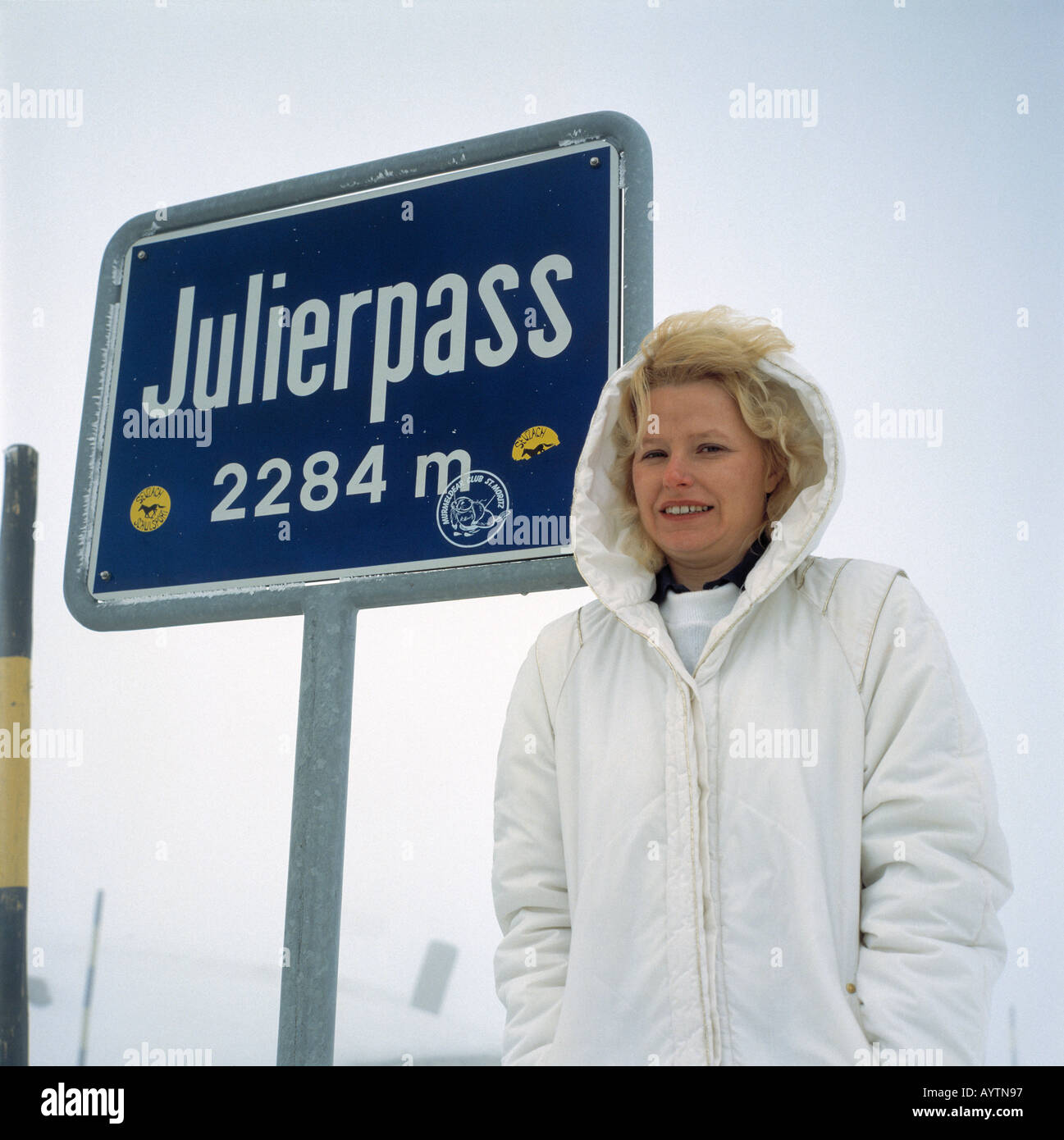 junge Frau posiert fuer Erinnerungsfoto vor Hinweisschild 'Julierpass', Graubuendener Alpen, Kanton Graubuenden Stock Photo