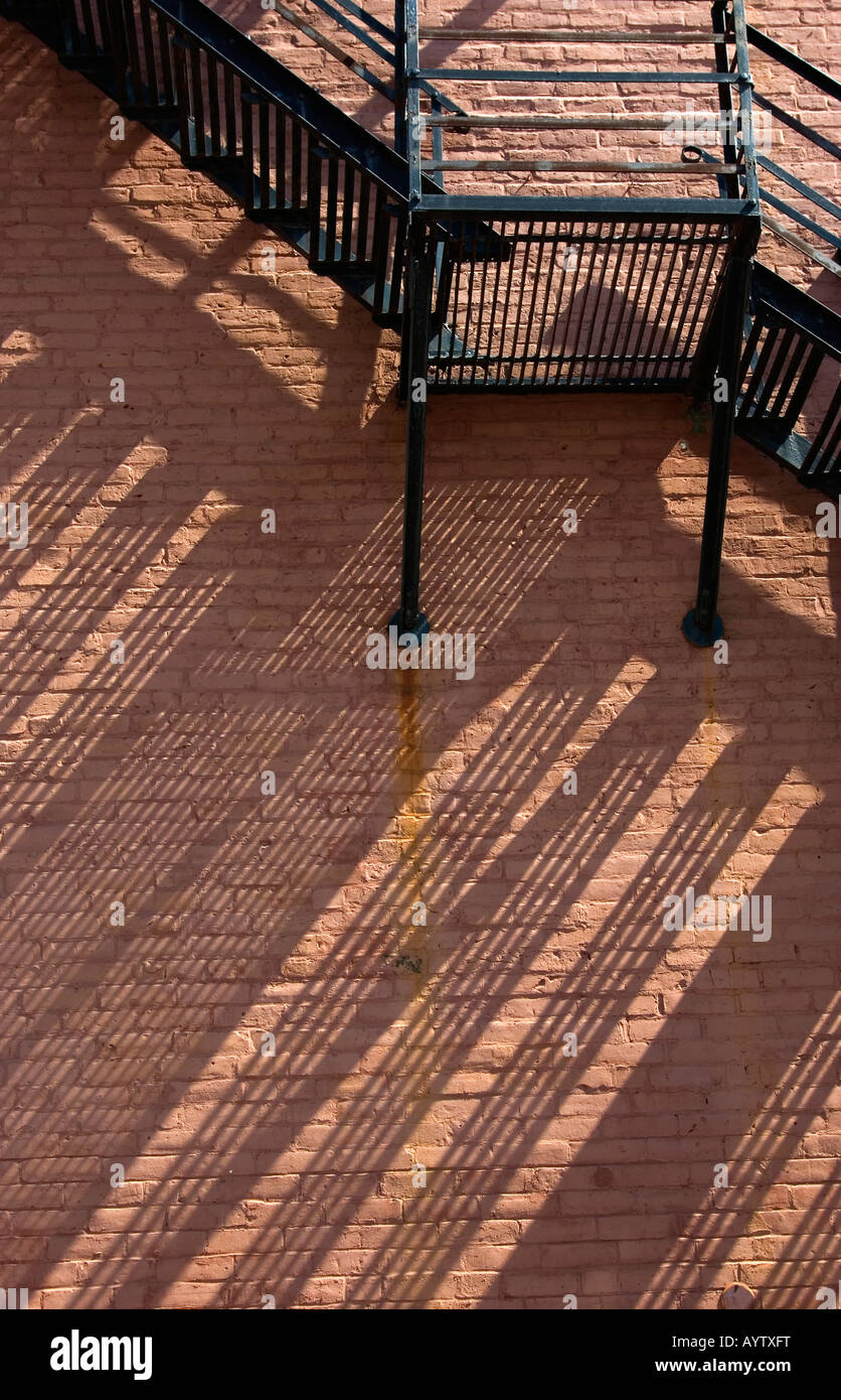 Metal fire escape stairway with slanting shadows on brick wall Stock Photo