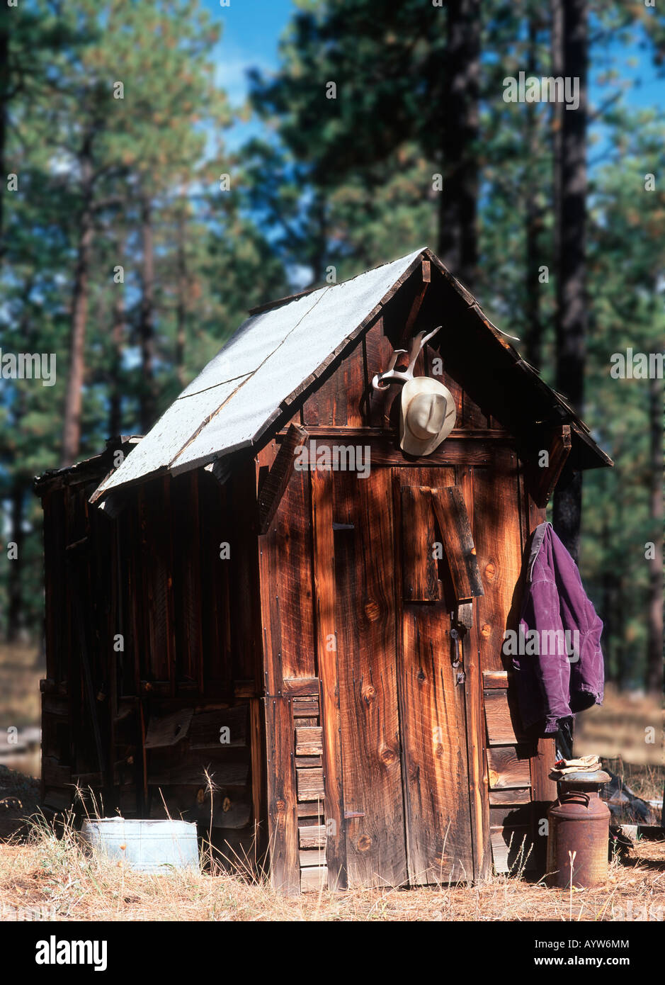 Cowboy hat hangs above a rural outhouse (water closet) signifying the toilet is in use. Stock Photo