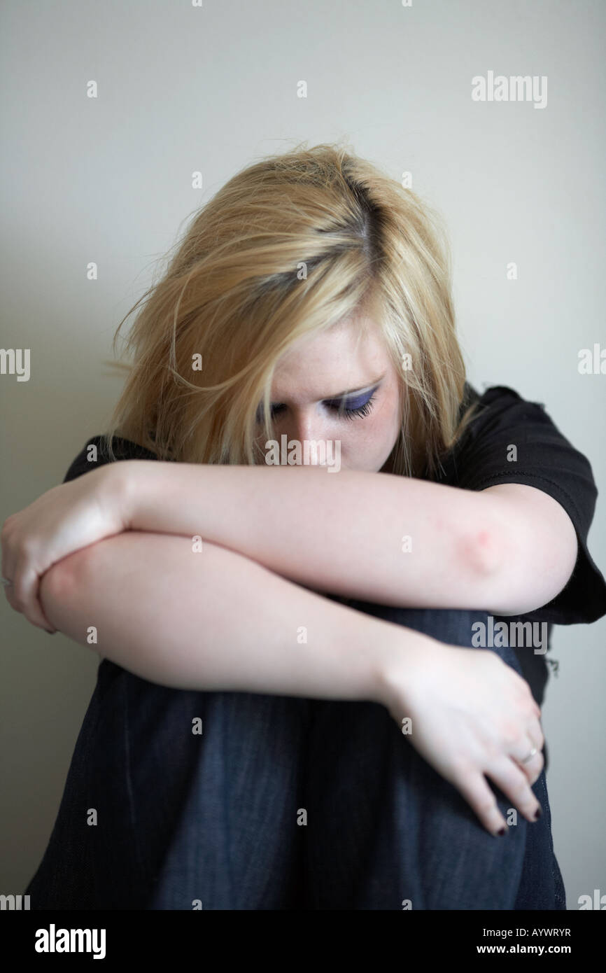 close up of arms and shoulders of blonde haired teenage woman sitting on floor with back to the wall Stock Photo