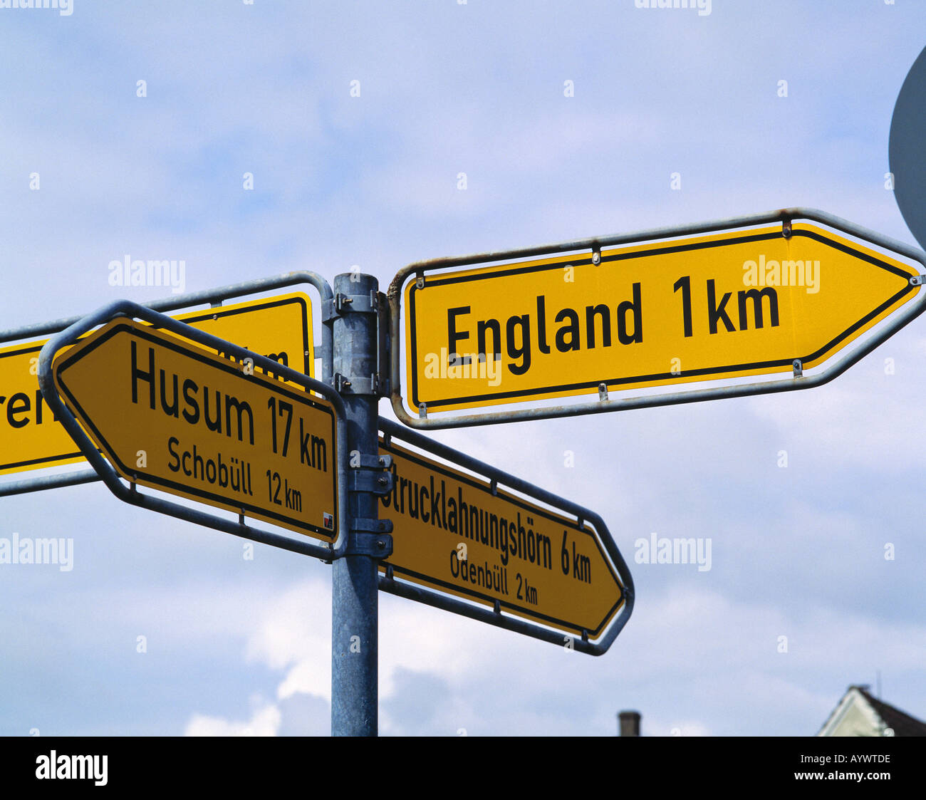 D-Nordstrand, North Sea, Schleswig-Holstein, road signs, direction signs on a crossroads showing to different towns and cities, intersection, Husum, Strucklahnungshoern, Schobuell, Odenbuell, England, funny sign shows a distance of one kilometer to reach Stock Photo