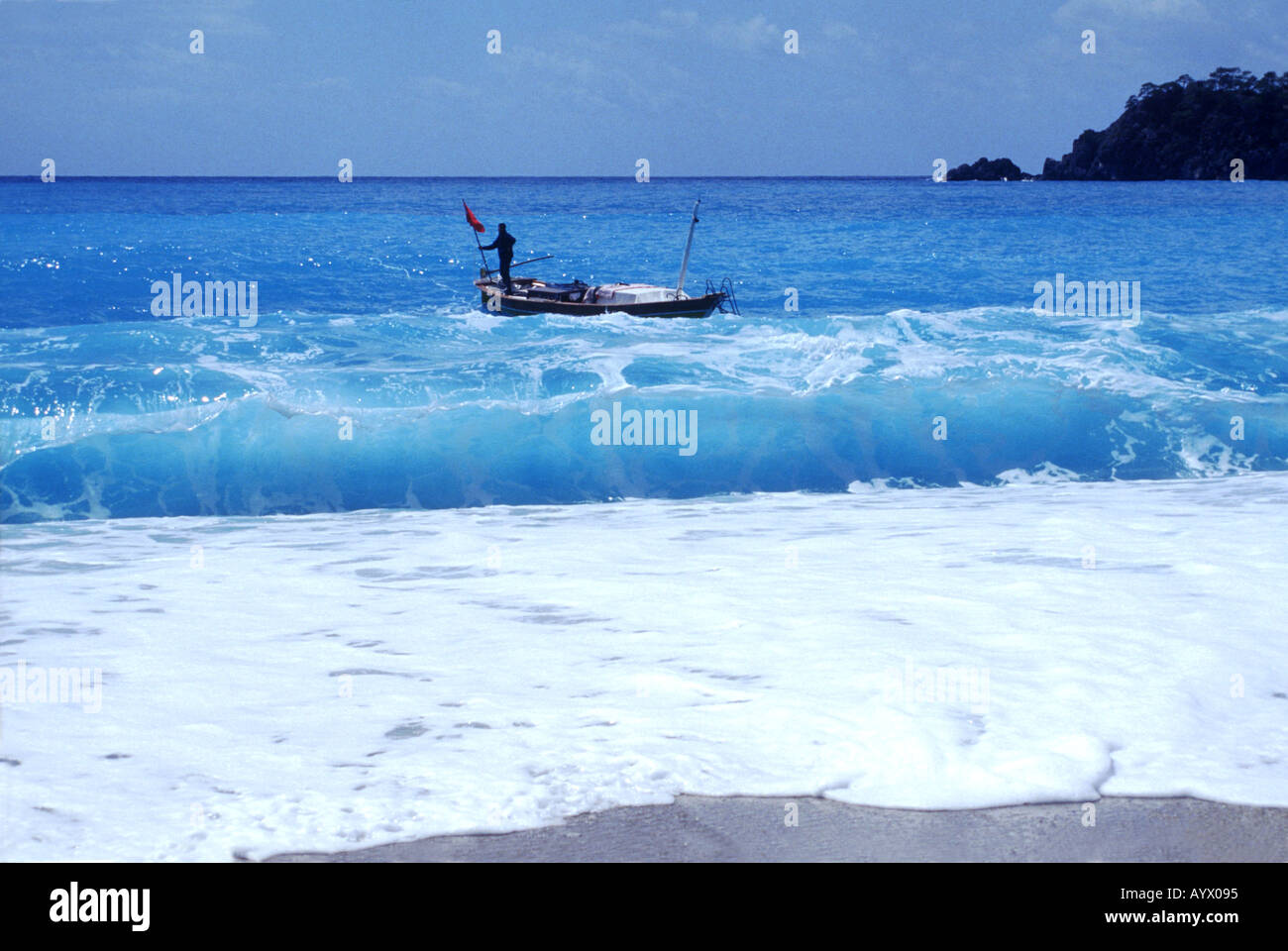 Light blue water white foam breaking waves on sandy Mediterranean beach fishermen standing on wooden boat. Stock Photo