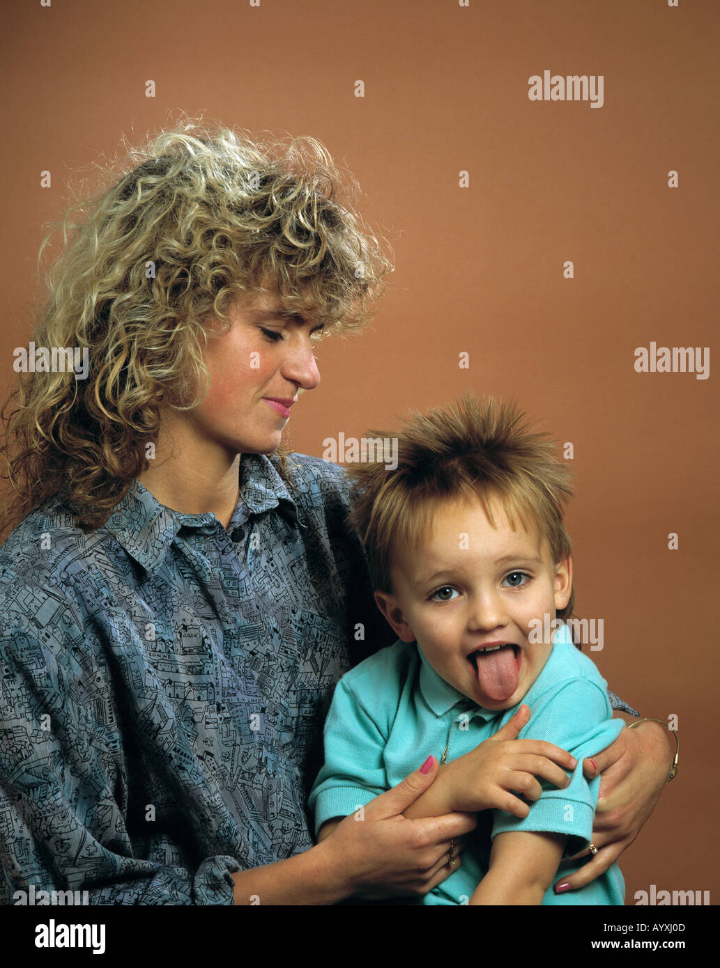 kleiner Junge auf dem Schoss der Mutter zeigt dem Fotografen die Zunge Stock Photo