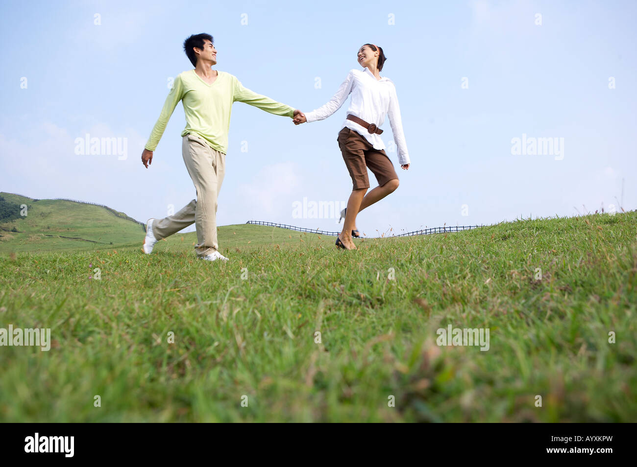 a couple grasping hands each other and walking on the grassfield Stock Photo