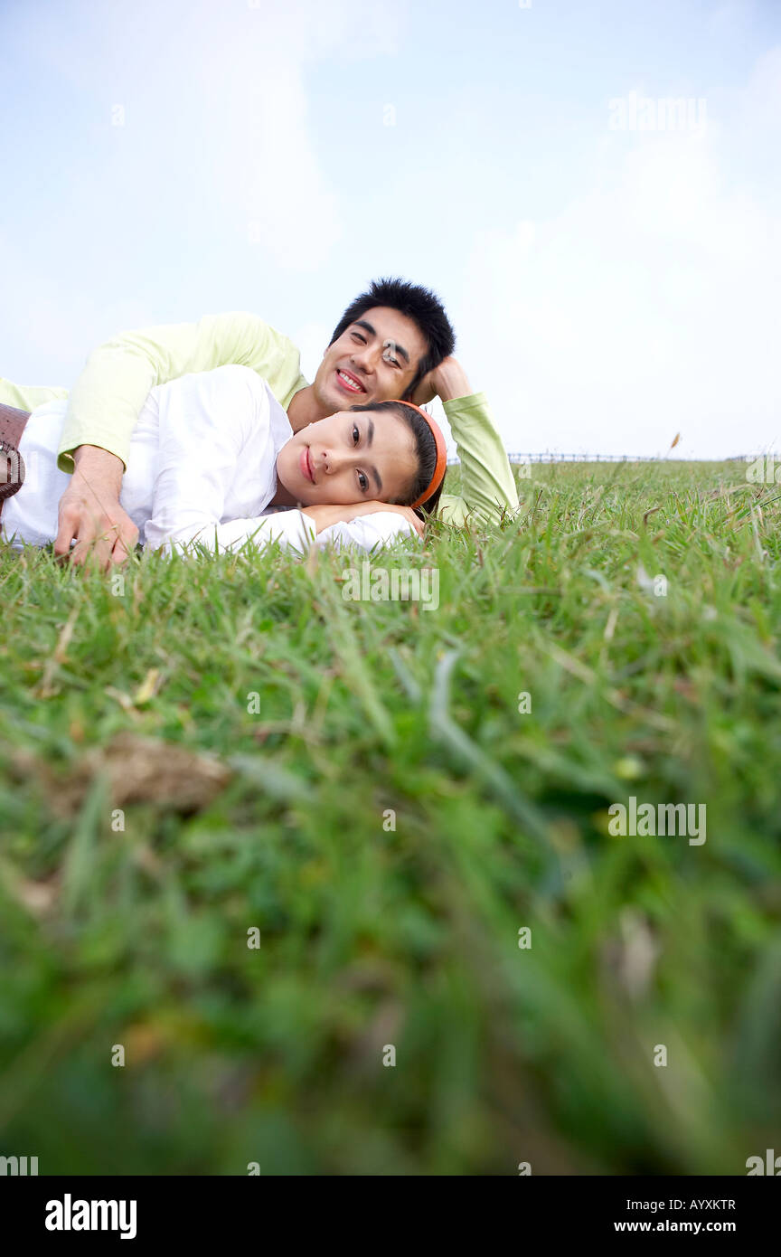 a couple laid with holding hands each other on the grass field Stock Photo