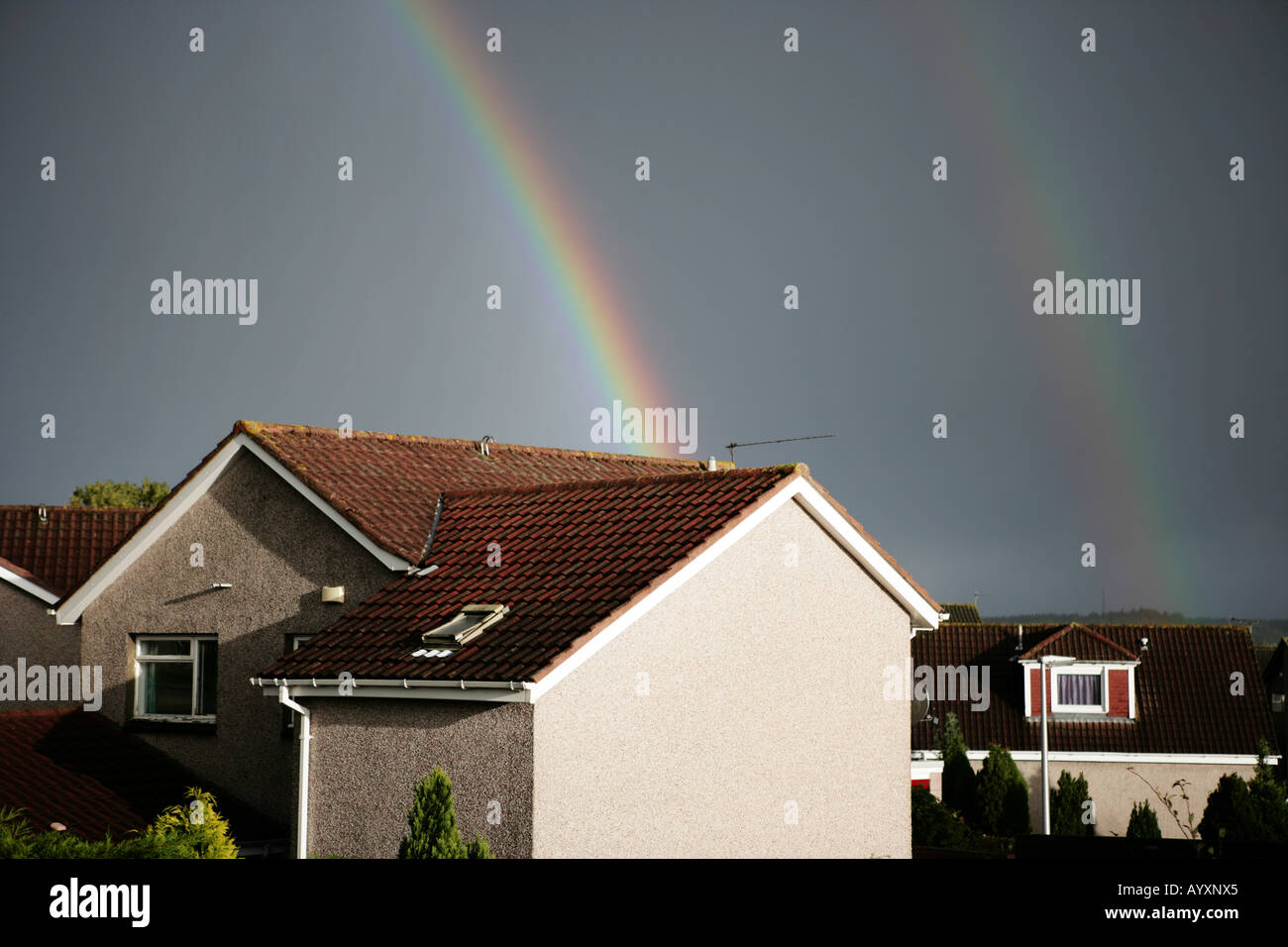 Two rainbows leading into two residential houses against a dark moody sky. Stock Photo