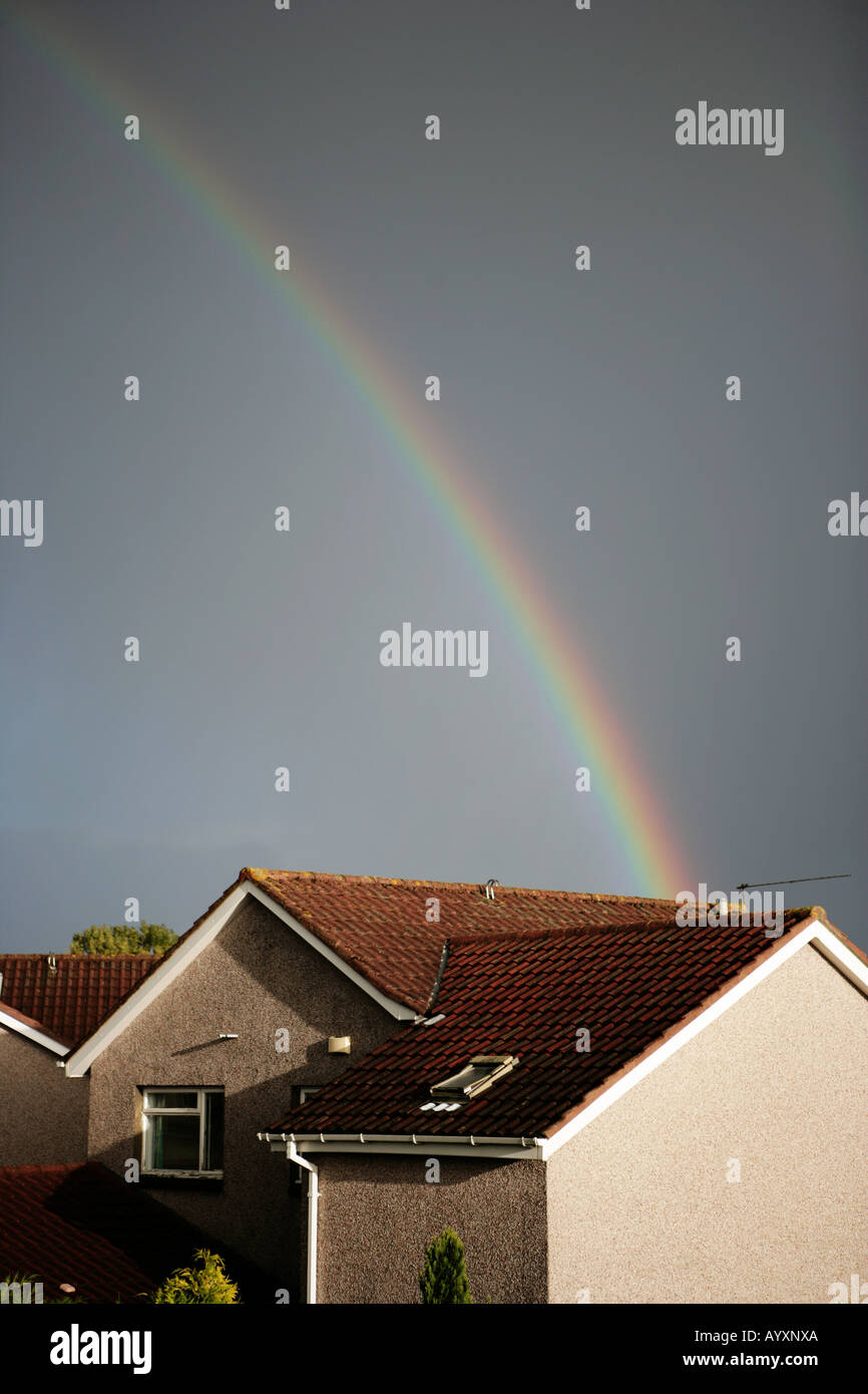 A single multi coloured rainbow leading into a single residential house with dark moody skies. Stock Photo