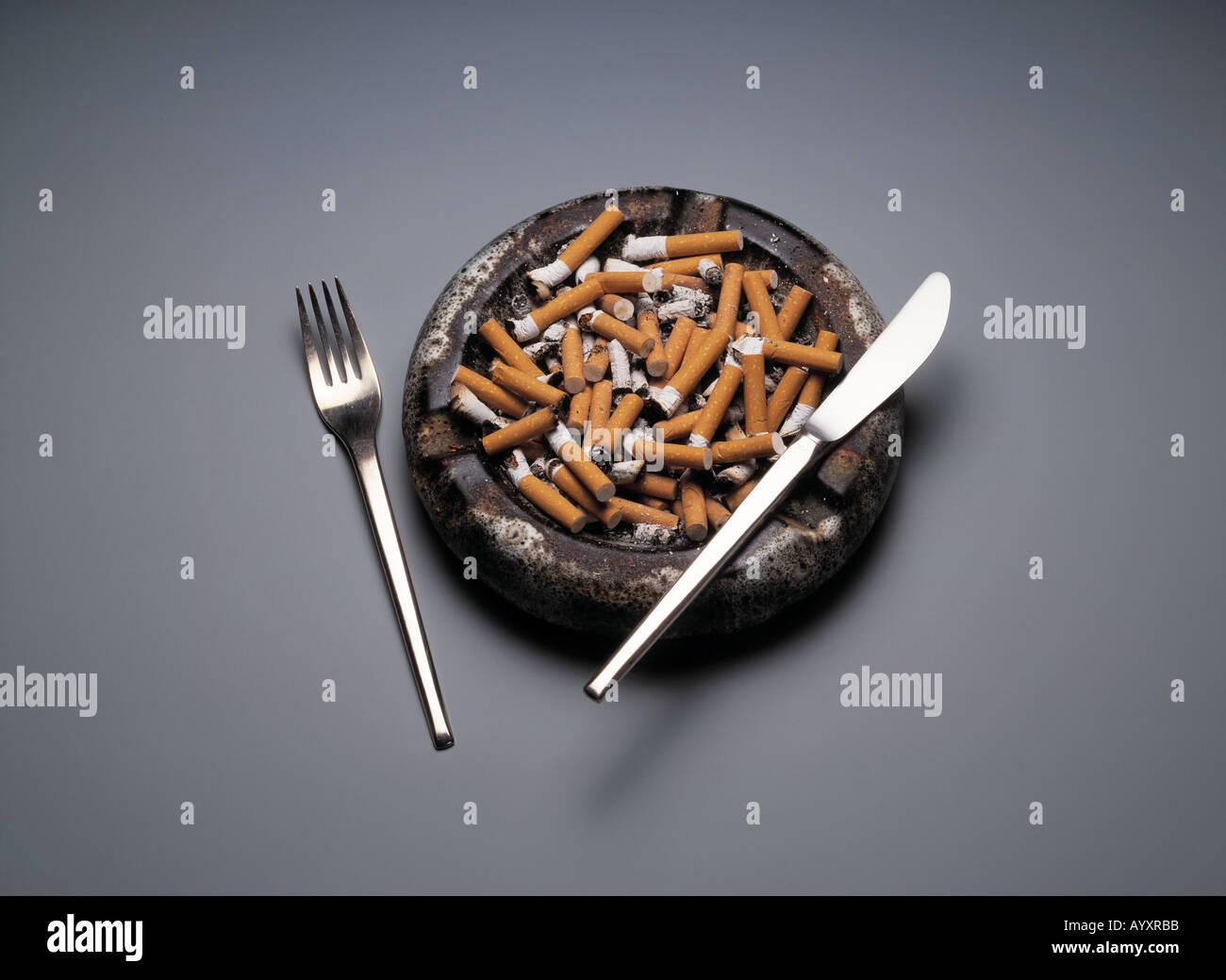 health, full ashtray, overcrowded, butts, stubs, smoking, knife and fork on the ashtray, revulsion, disgust, give up smoking Stock Photo